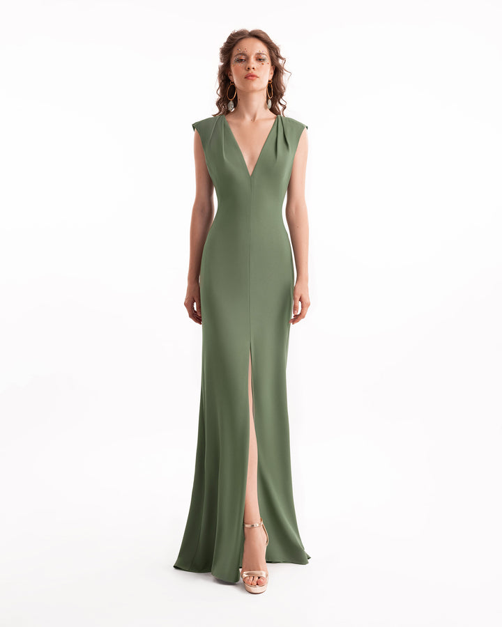 Woman wearing a green evening gown with a deep neckline and slit on a white background