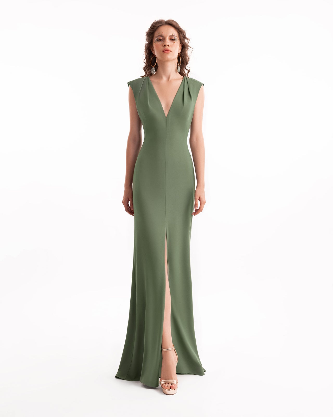 Woman wearing a green evening gown with a deep neckline and slit on a white background