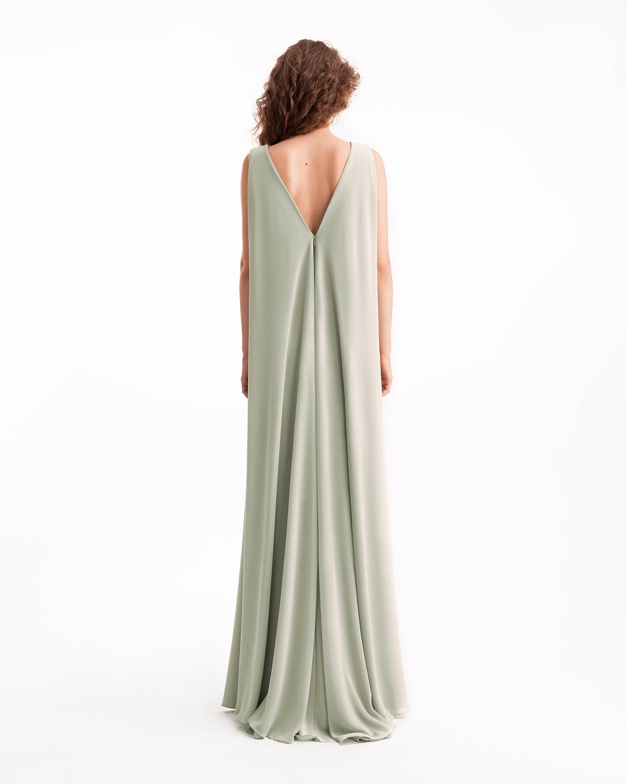 Woman wearing a long, light green dress with a backless design on a white background