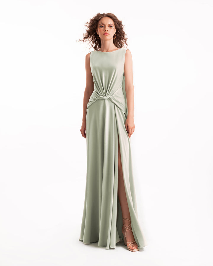 Woman wearing a light green evening gown with a slit on a white background