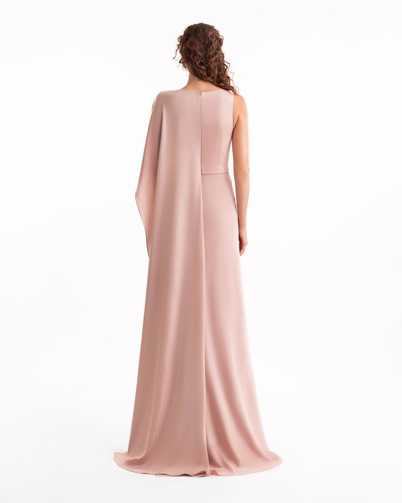 Woman wearing a long, light pink dress with a cape on a white background