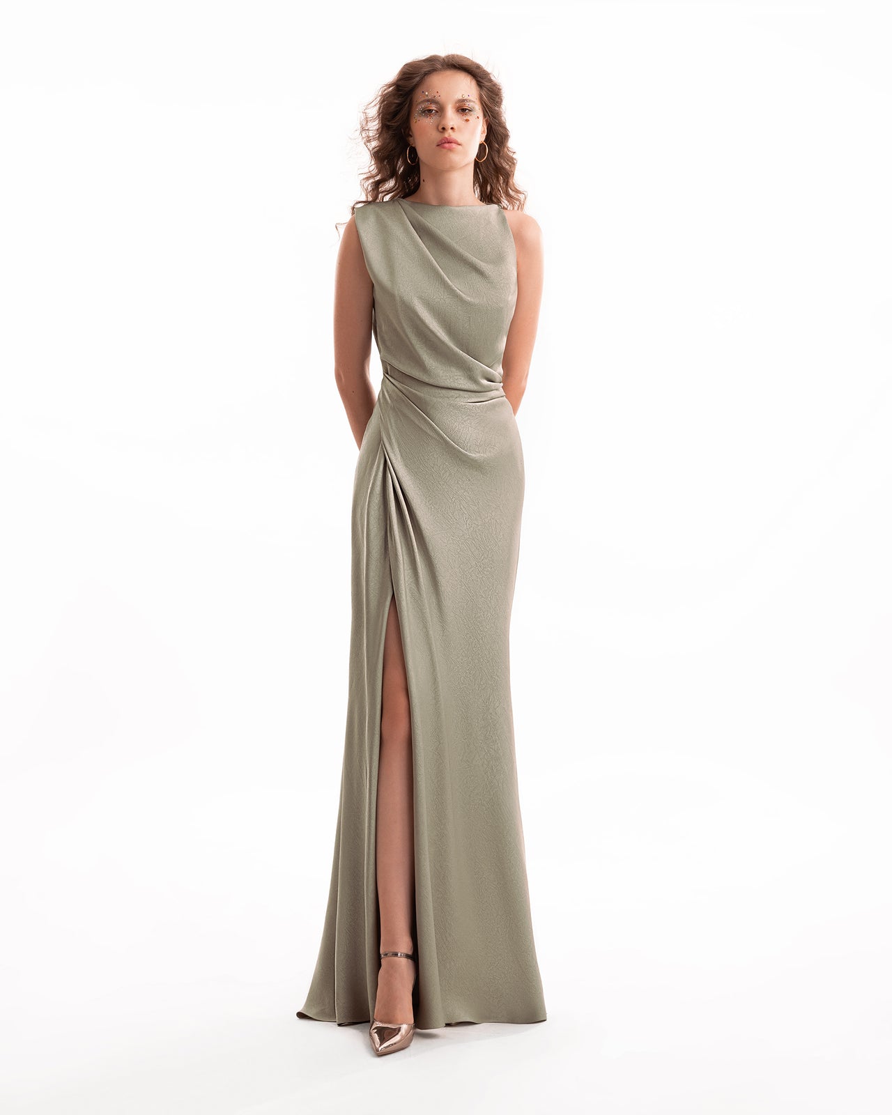 Woman wearing a long, sleeveless olive green dress with a slit on a white background