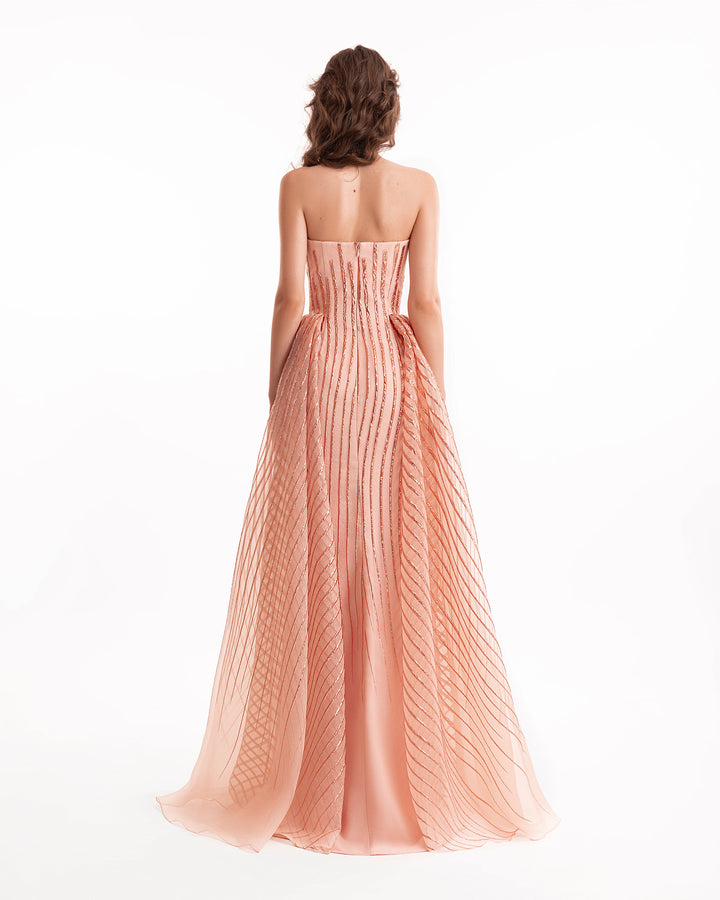 Woman wearing a strapless, pleated pink gown on a white background
