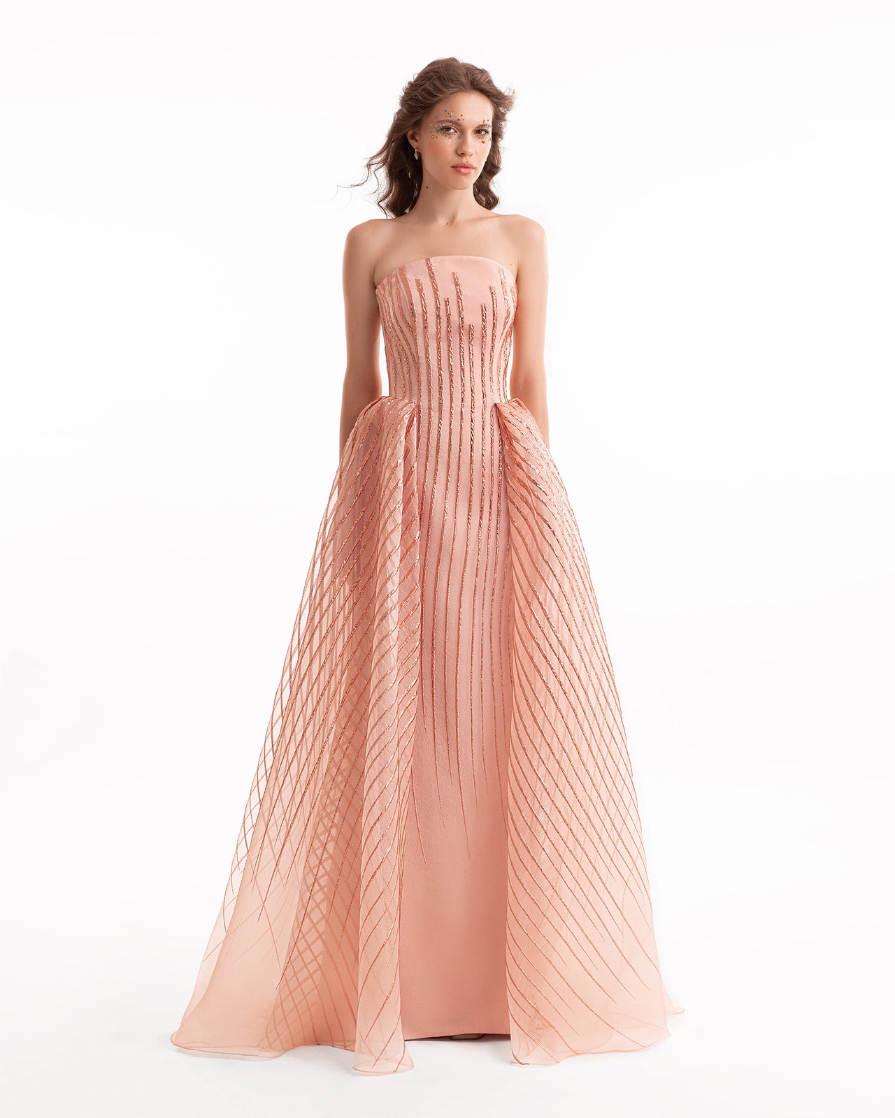 Woman wearing a strapless, long, pleated pink dress on a white background