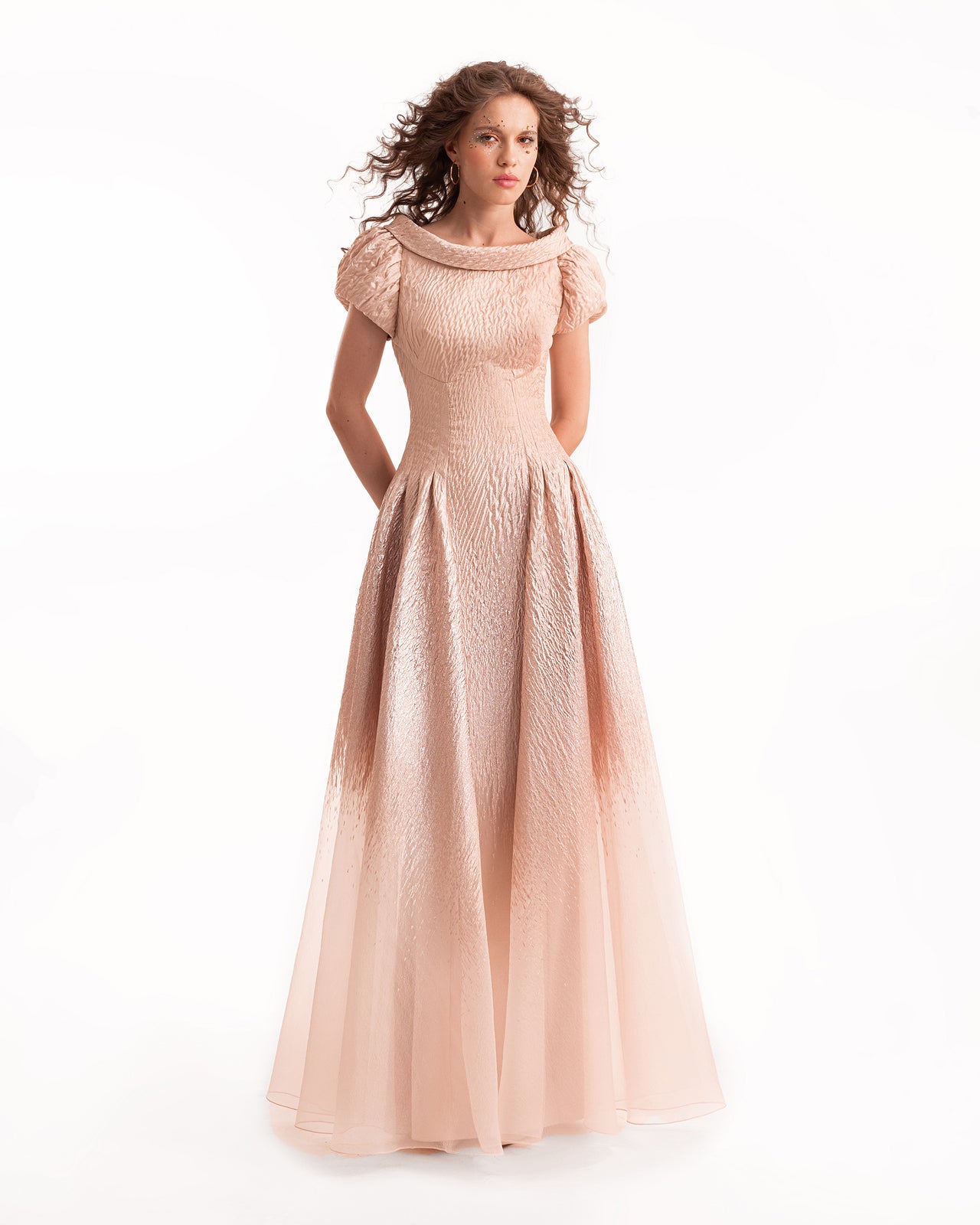 Woman wearing a long, light pink dress with a textured pattern on a white background