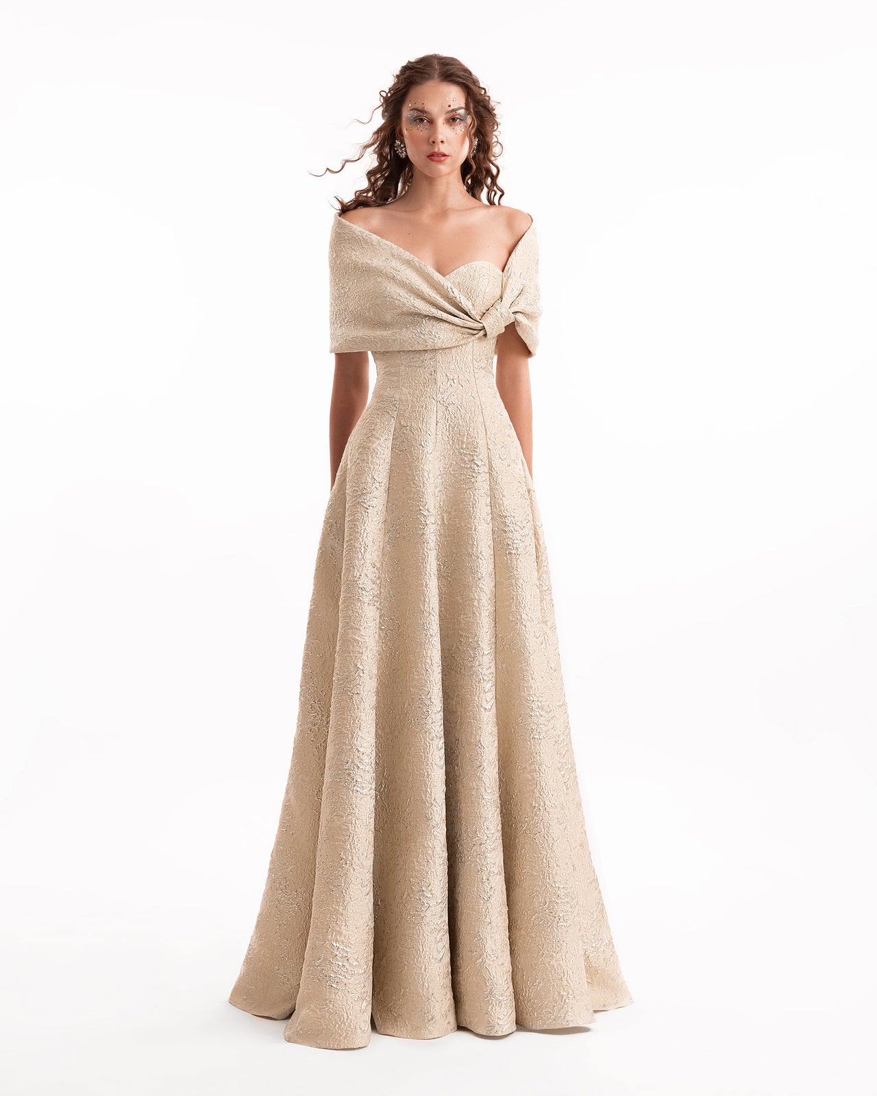 Woman wearing a beige off-shoulder evening gown on a white background