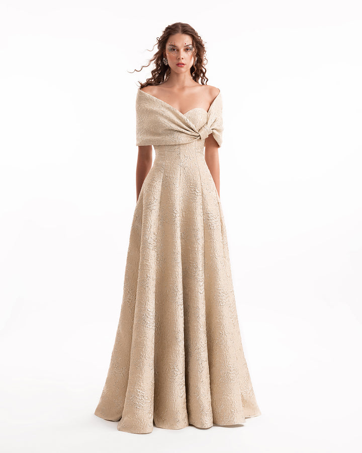 Woman wearing a beige off-shoulder evening gown on a white background