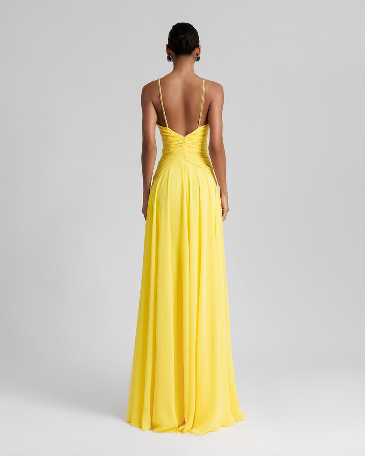 The back of a long yellow evening dress featuring draping on the waist, beaded straps and an open back.