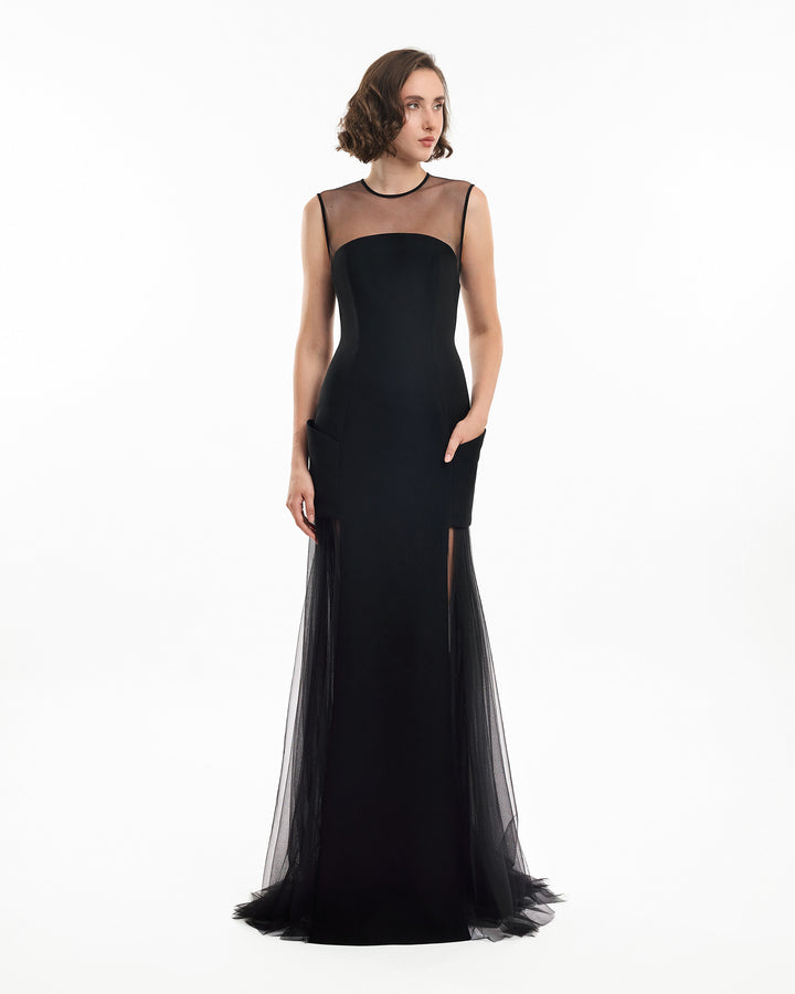 Woman wearing a black evening gown with sheer overlay on a white background