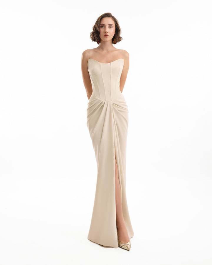 Woman wearing a strapless, floor-length beige dress on a white background