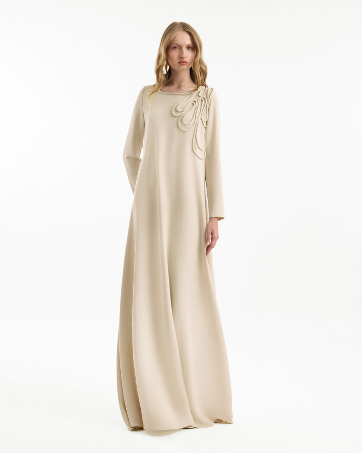 Woman wearing a beige long dress with floral details on a white background