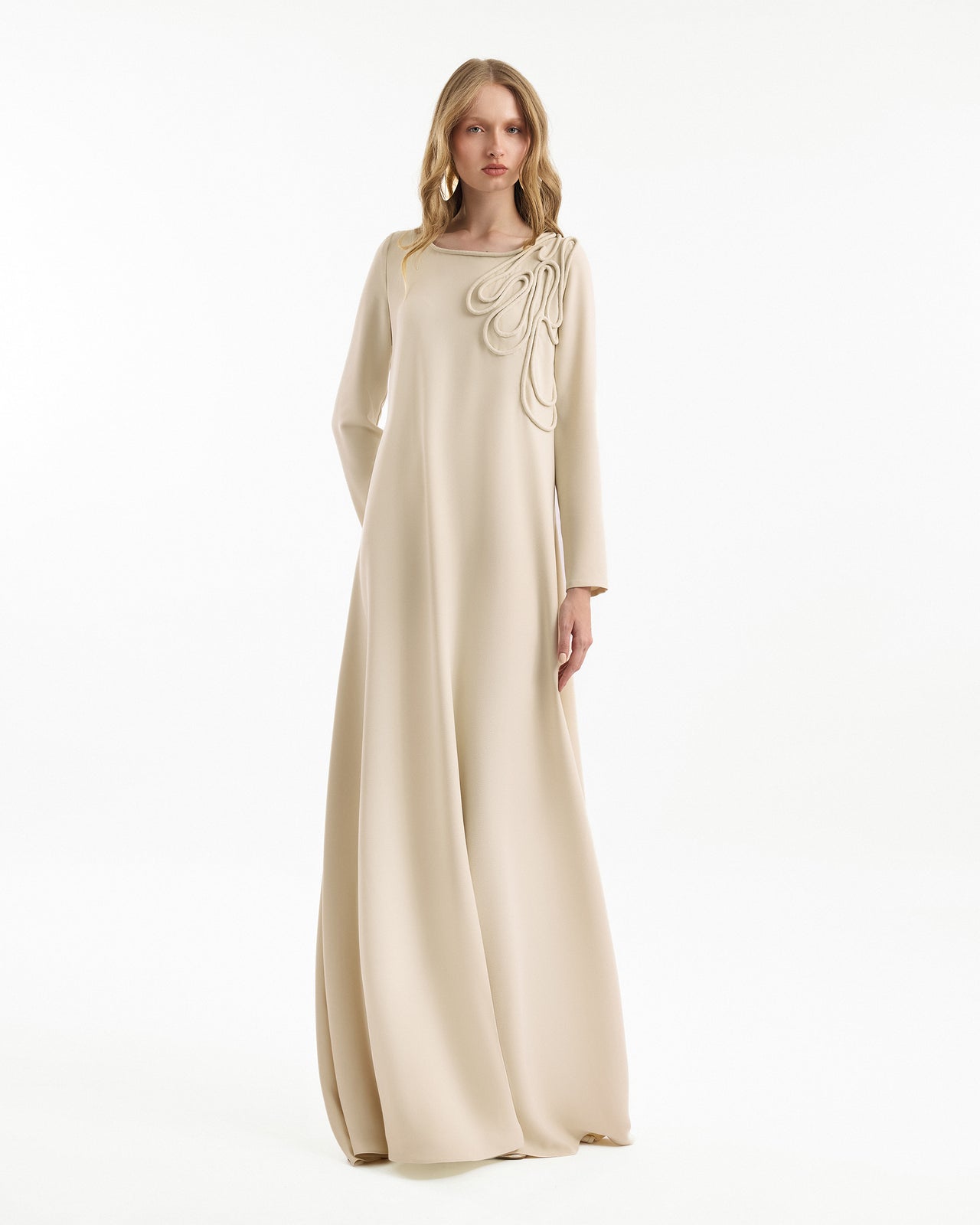 Woman wearing a beige long dress with floral details on a white background