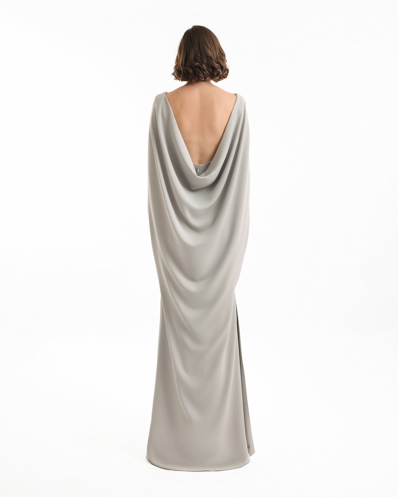 Woman wearing a silver evening gown with a draped back design on a white background