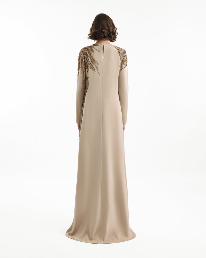 Beige evening gown with intricate shoulder detailing on a white background