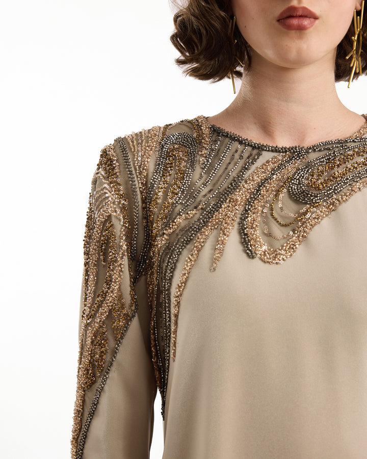 Close-up of a beige dress with intricate beaded detailing on a white background