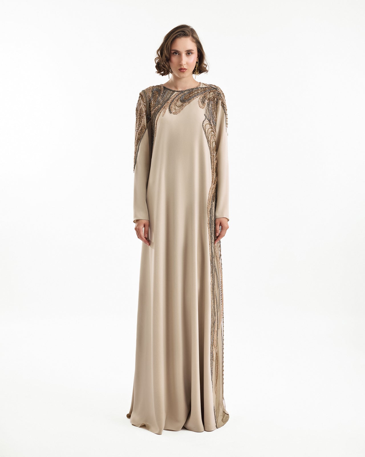 Woman wearing a long, elegant dress with intricate detailing on a white background