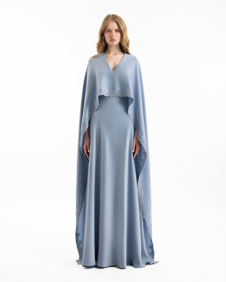 Woman wearing a light blue evening gown with a cape on a white background