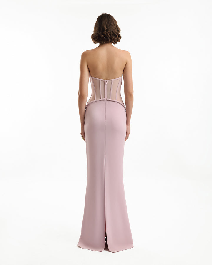 Woman wearing a pink strapless gown with a high slit on a white background