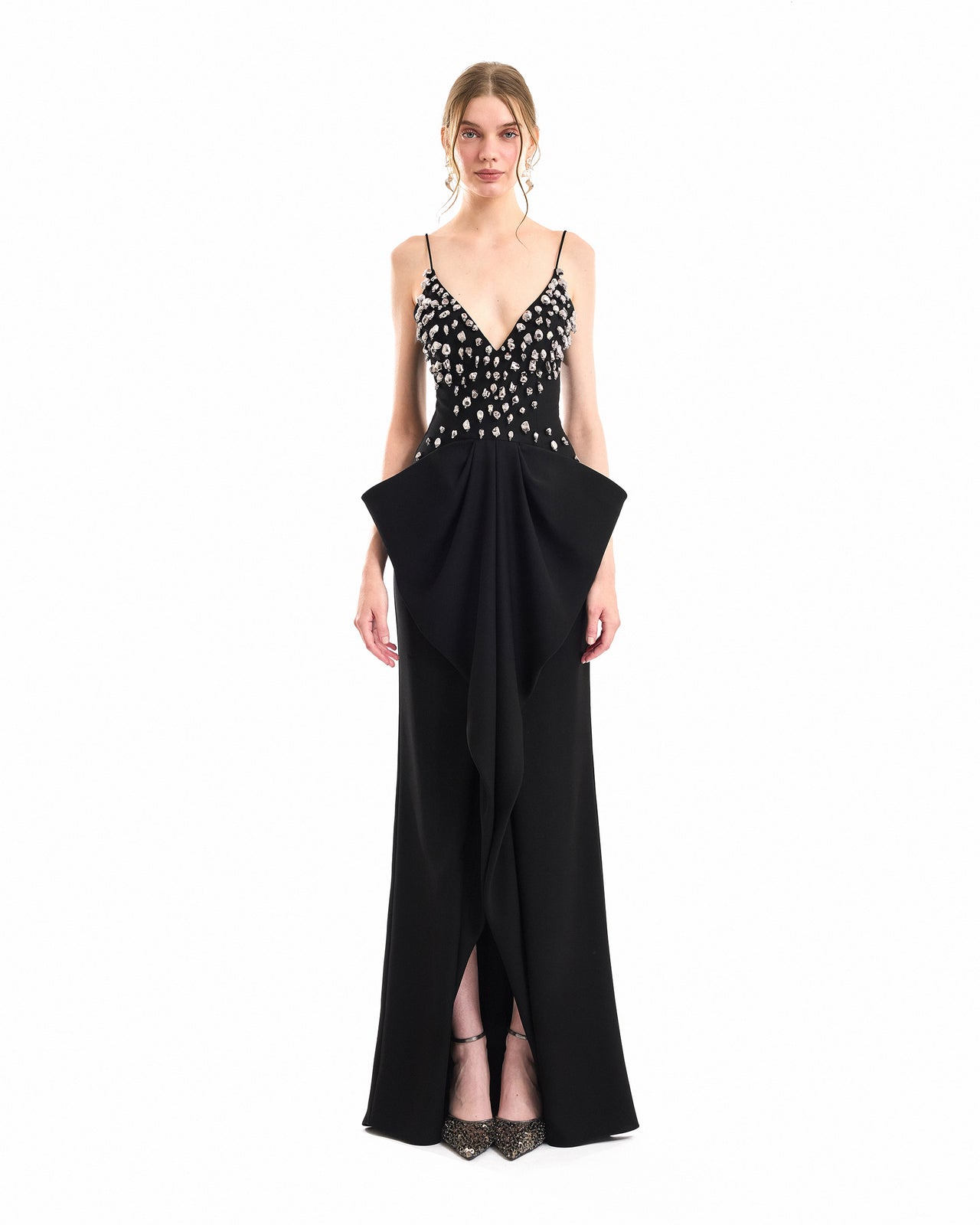 A model wearing a black floor-length gown with a beaded bodice, thin spaghetti straps, and a dramatic draped skirt detail, photographed against a solid white background.