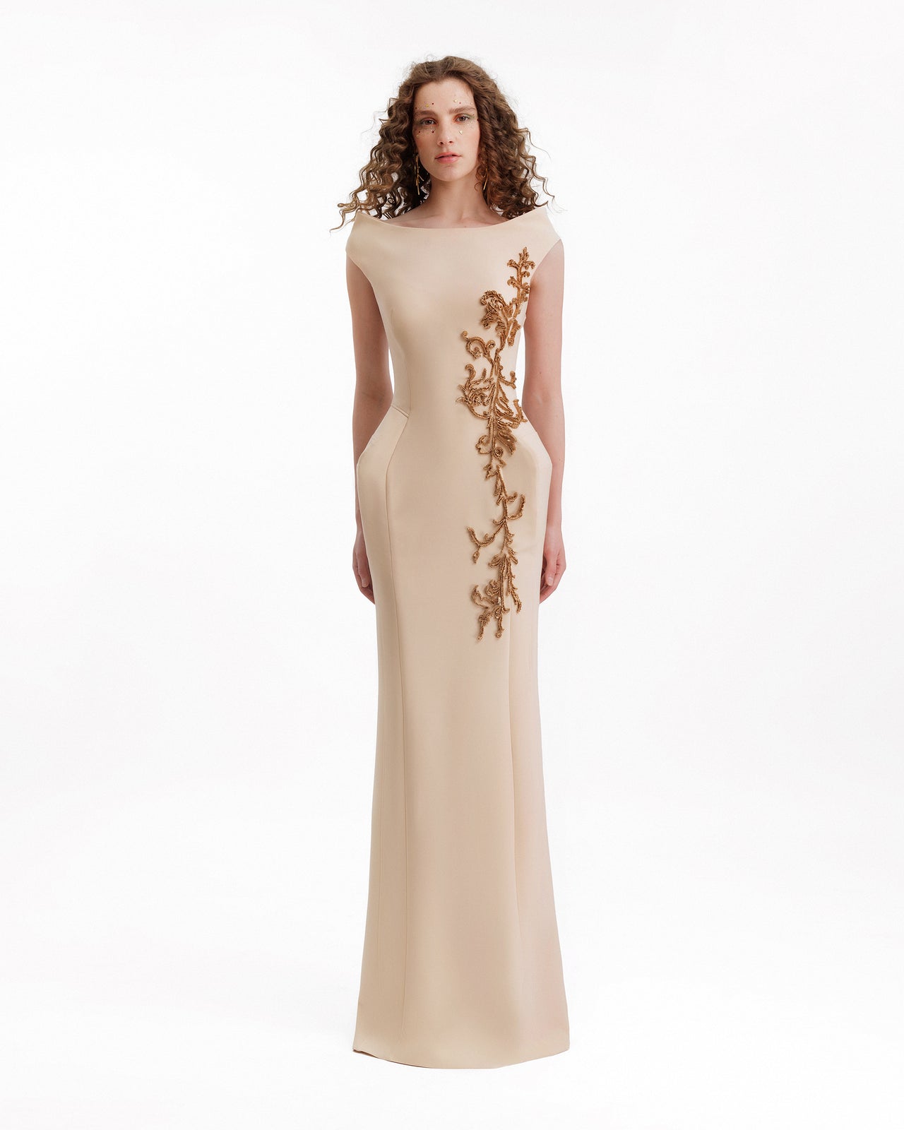 Woman wearing a beige evening gown with gold embroidery on a white background