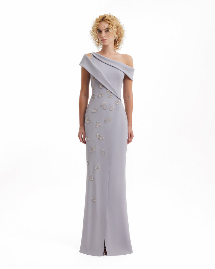 Woman wearing a gray one-shoulder evening gown with floral embellishments on a white background
