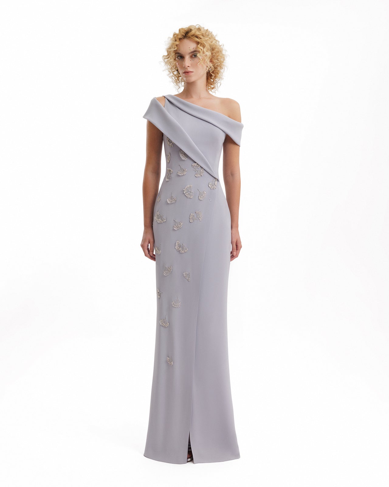 Woman wearing a gray one-shoulder evening gown with floral embellishments on a white background