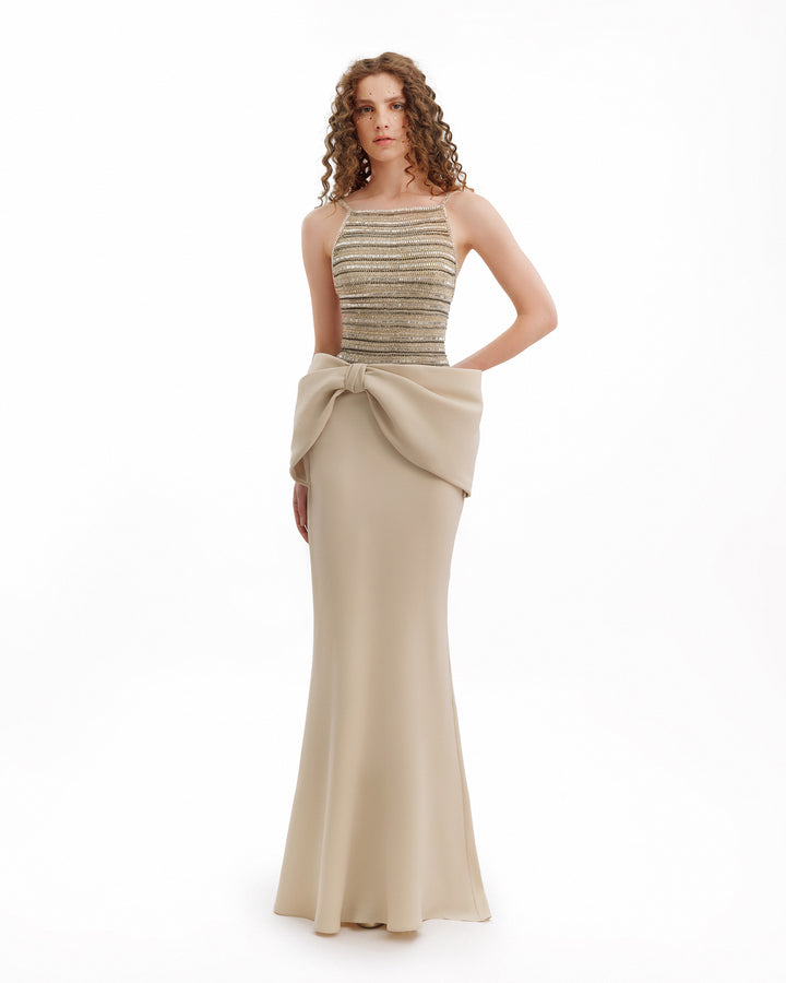 Woman wearing a halter neck dress with a draped beige skirt on a white background