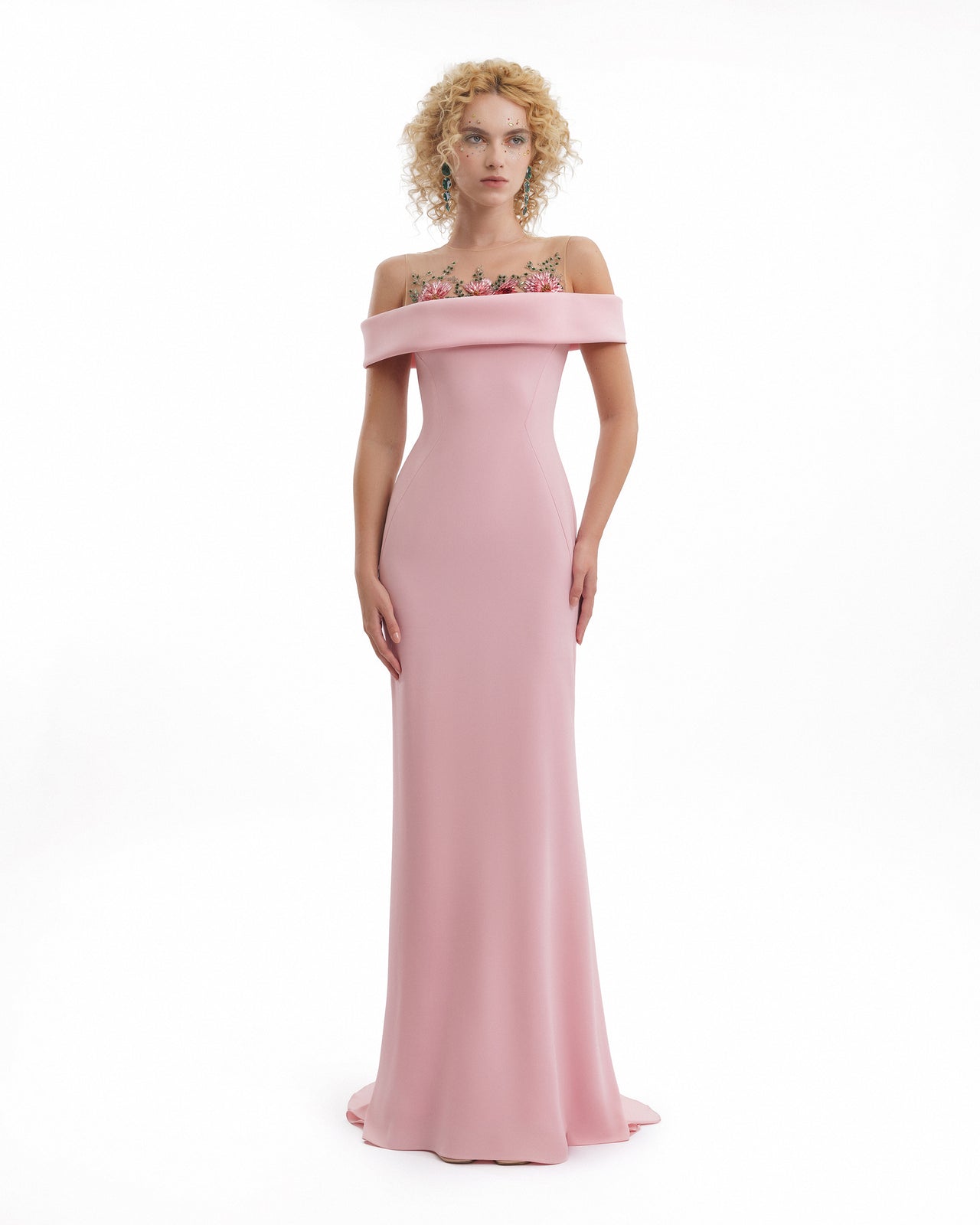 Woman wearing a pink off-shoulder gown with floral details on a white background