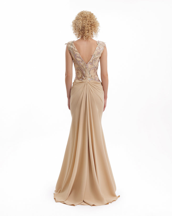 Woman wearing a beige evening gown with intricate lace detailing on a white background