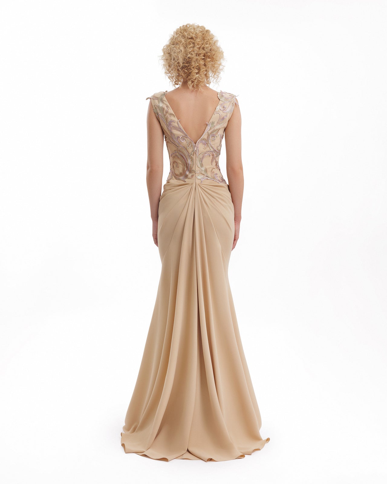 Woman wearing a beige evening gown with intricate lace detailing on a white background