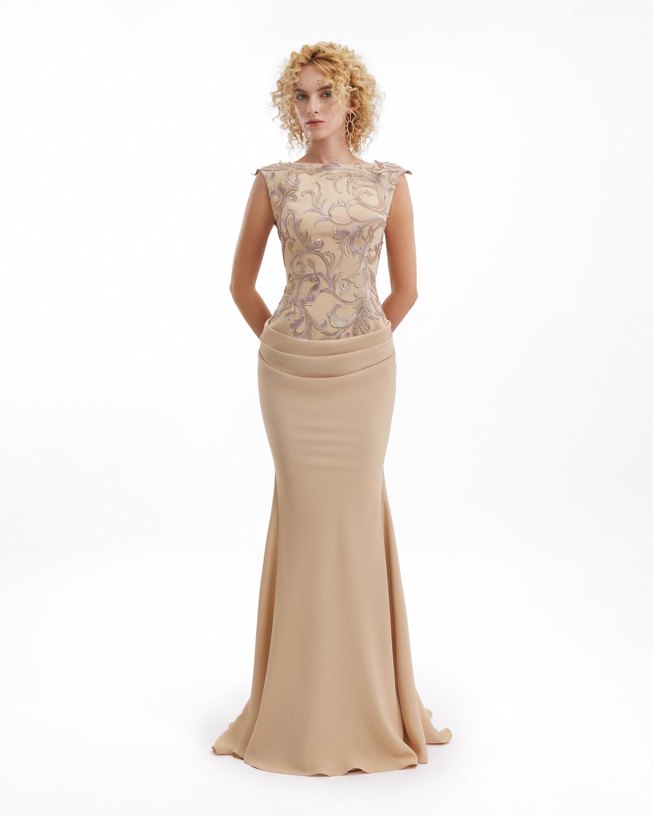 Woman wearing a beige evening gown with lace detailing on a white background