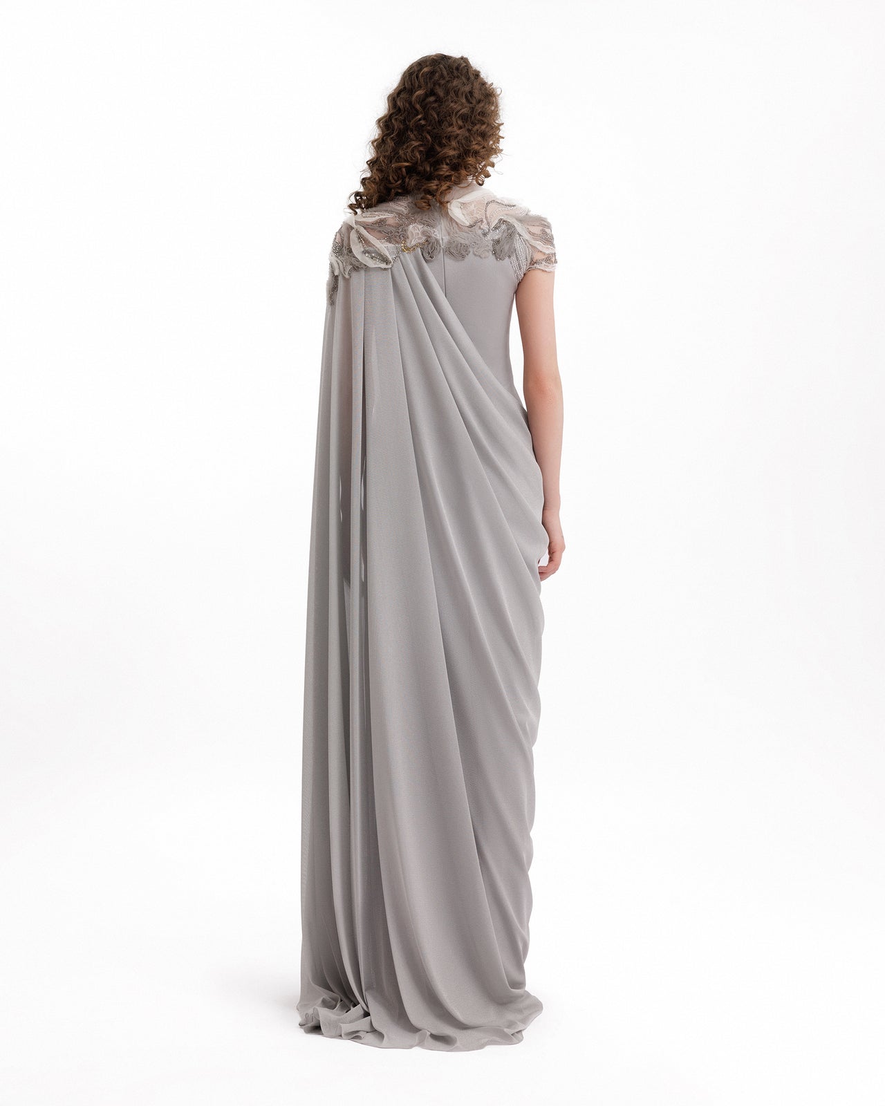 Woman wearing a long, elegant gray dress with lace details on a white background