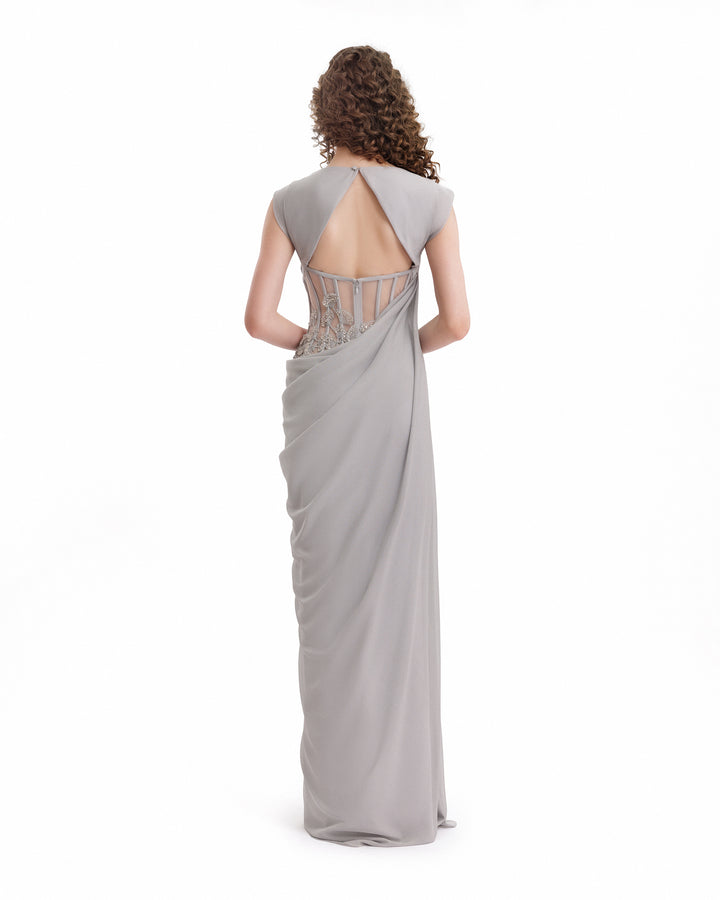 Woman wearing a silver evening gown with a sheer back on a white background