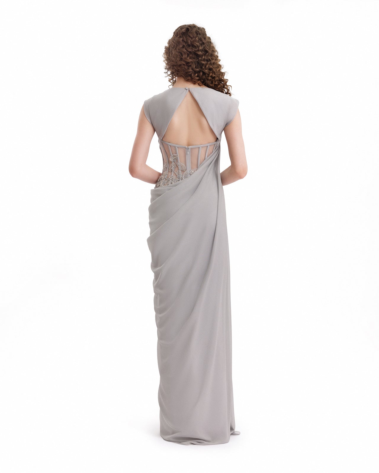 Woman wearing a silver evening gown with a sheer back on a white background