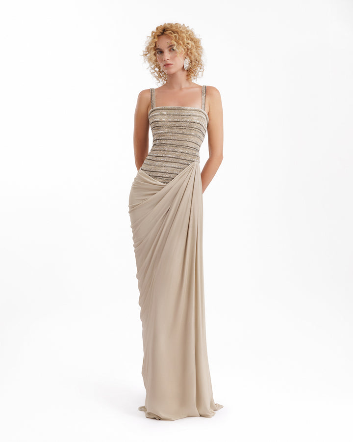 Woman wearing a beige evening gown with a draped effect on a white background