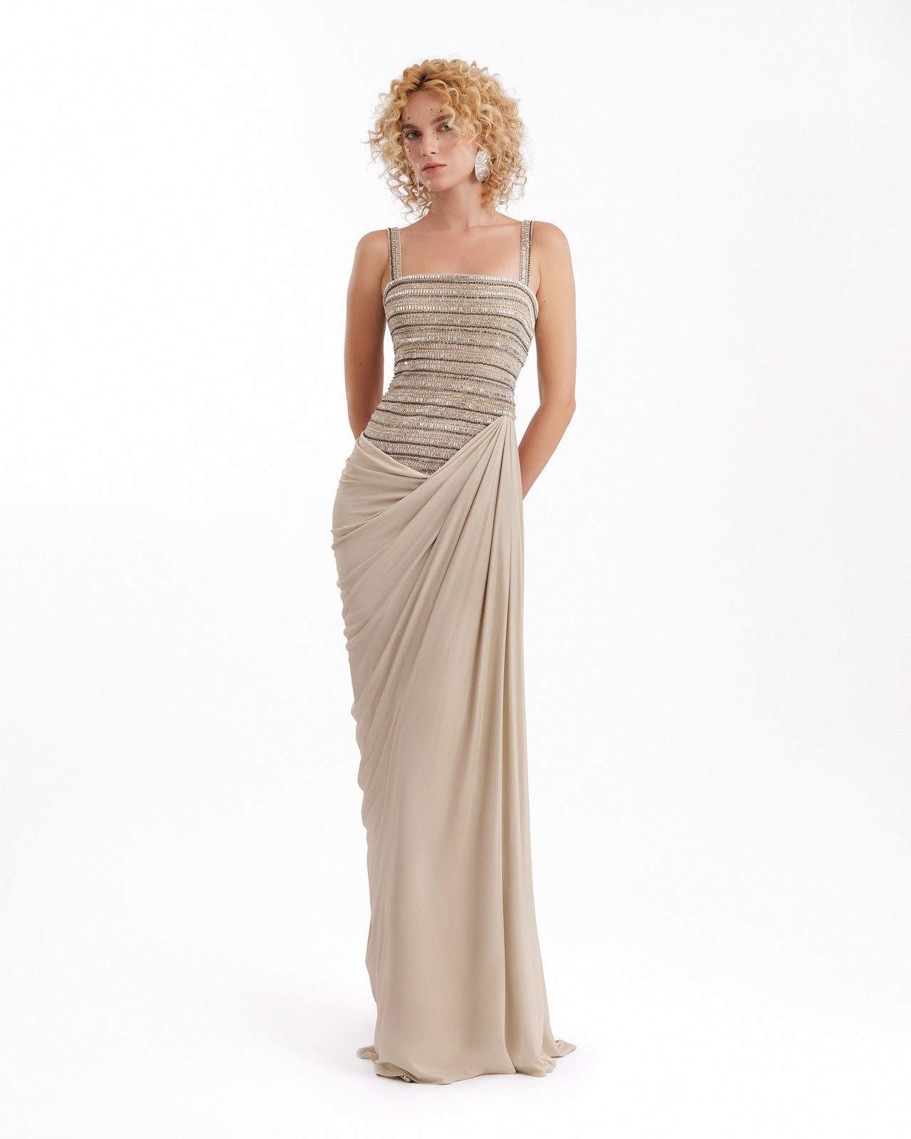 Woman wearing a beige evening gown with a draped effect on a white background