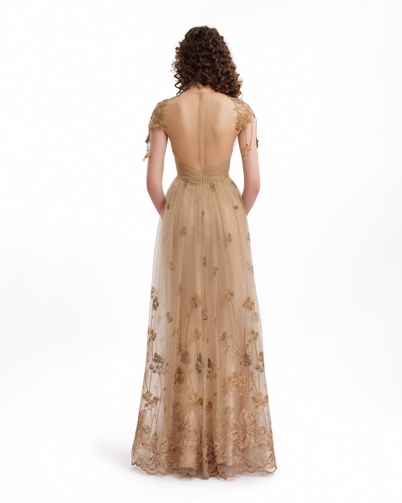 Woman wearing a beige evening gown with floral embroidery on a white background