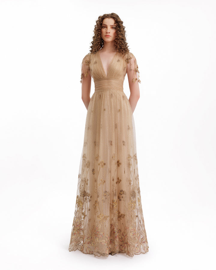 Woman wearing a beige evening gown with floral details on a white background