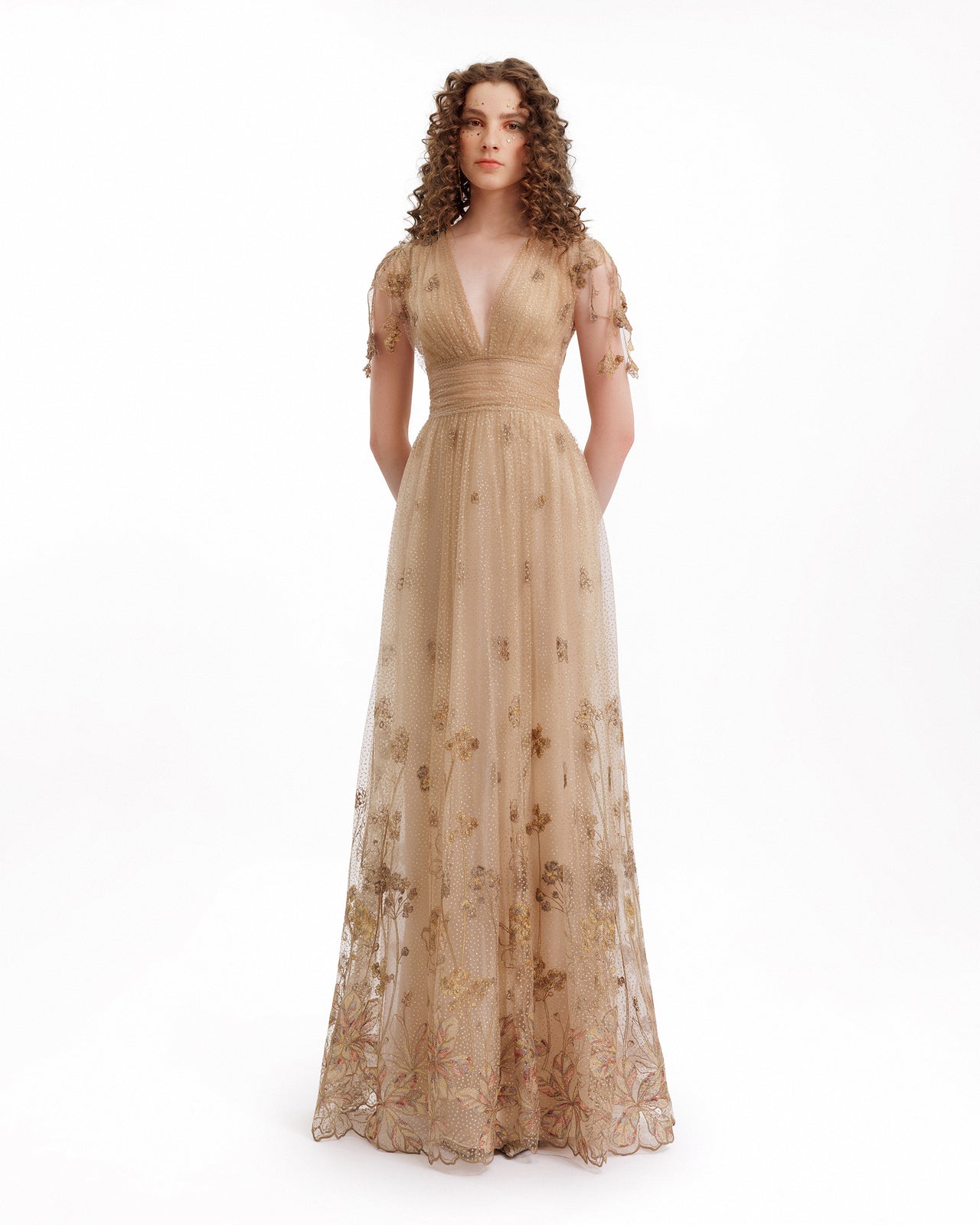 Woman wearing a beige evening gown with floral details on a white background