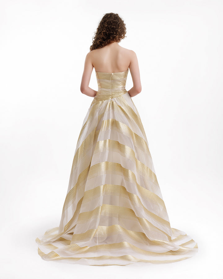 Woman wearing a gold and white striped evening gown on a white background