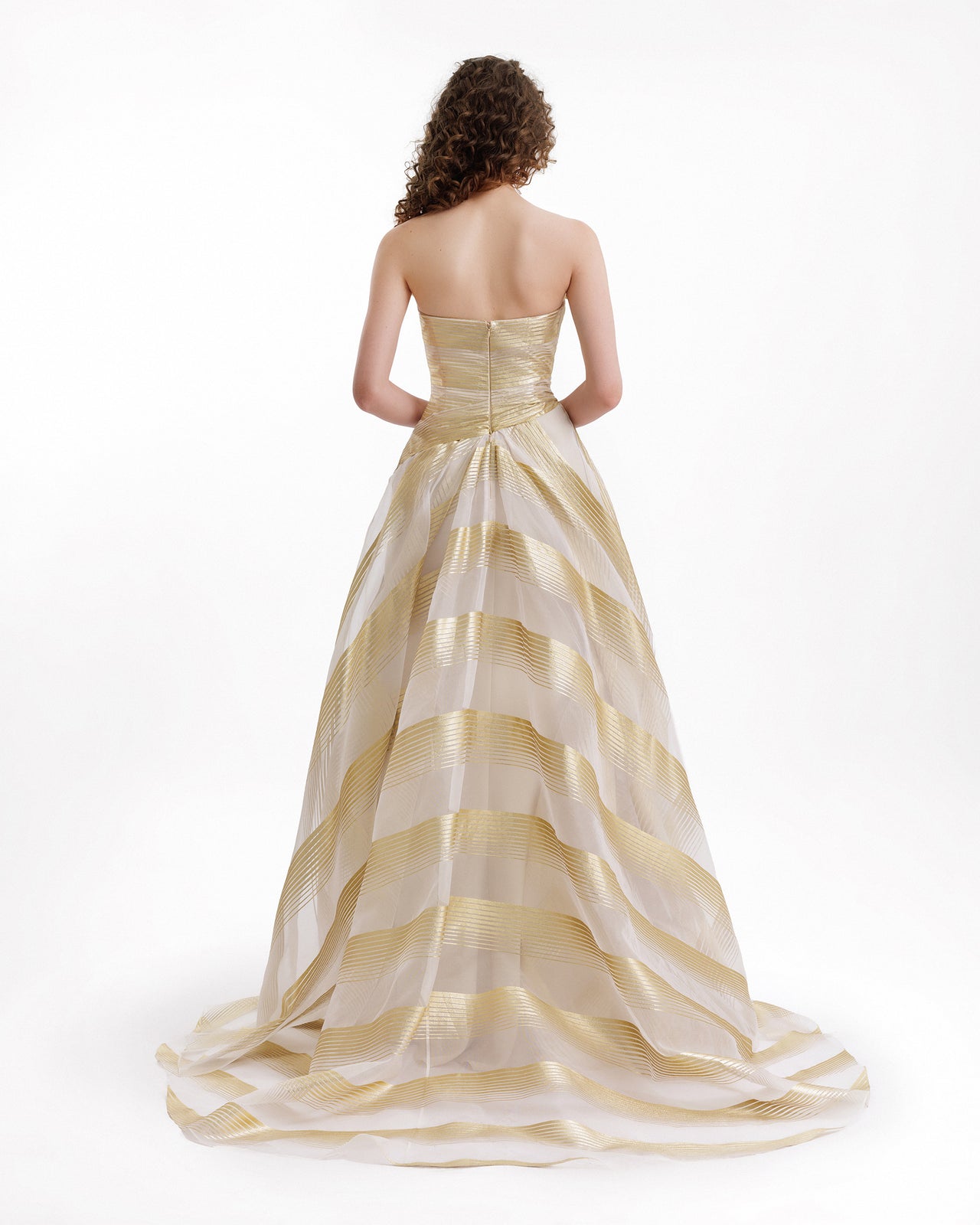 Woman wearing a gold and white striped evening gown on a white background