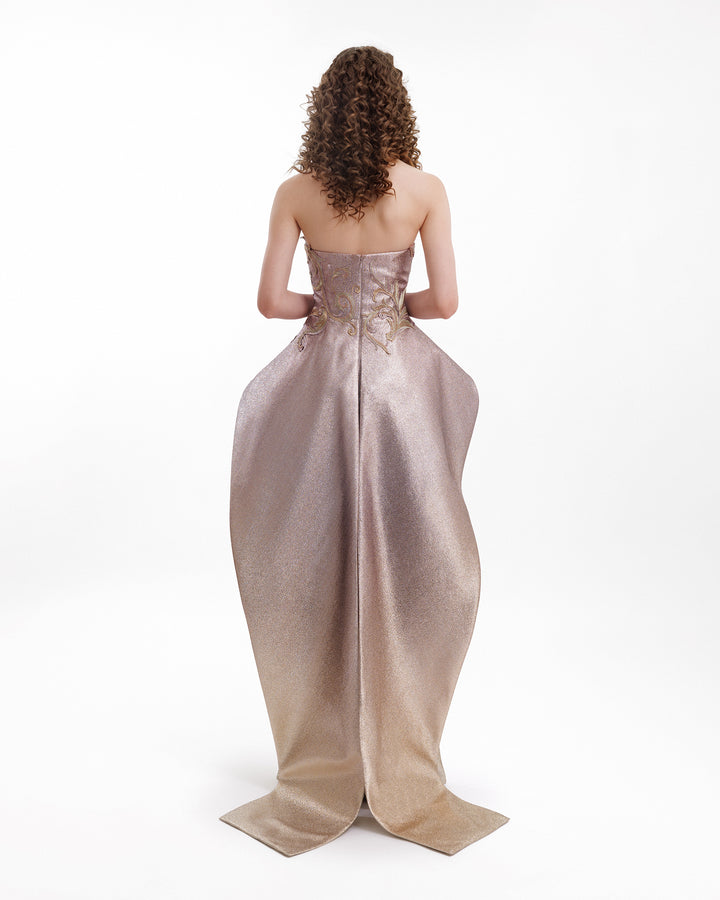 Woman wearing a strapless evening gown with intricate detailing on a white background