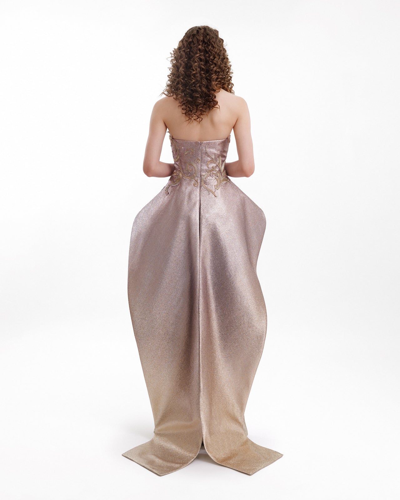 Woman wearing a strapless evening gown with intricate detailing on a white background