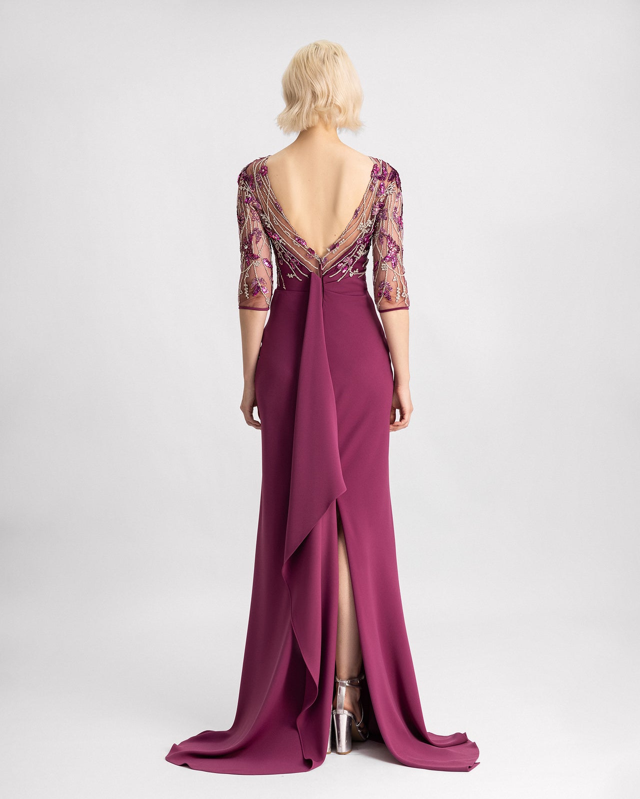 The back of a slim-cut evening dress in mulberry color with a beaded corset, three-quarter sleeves, and a slit at the back.