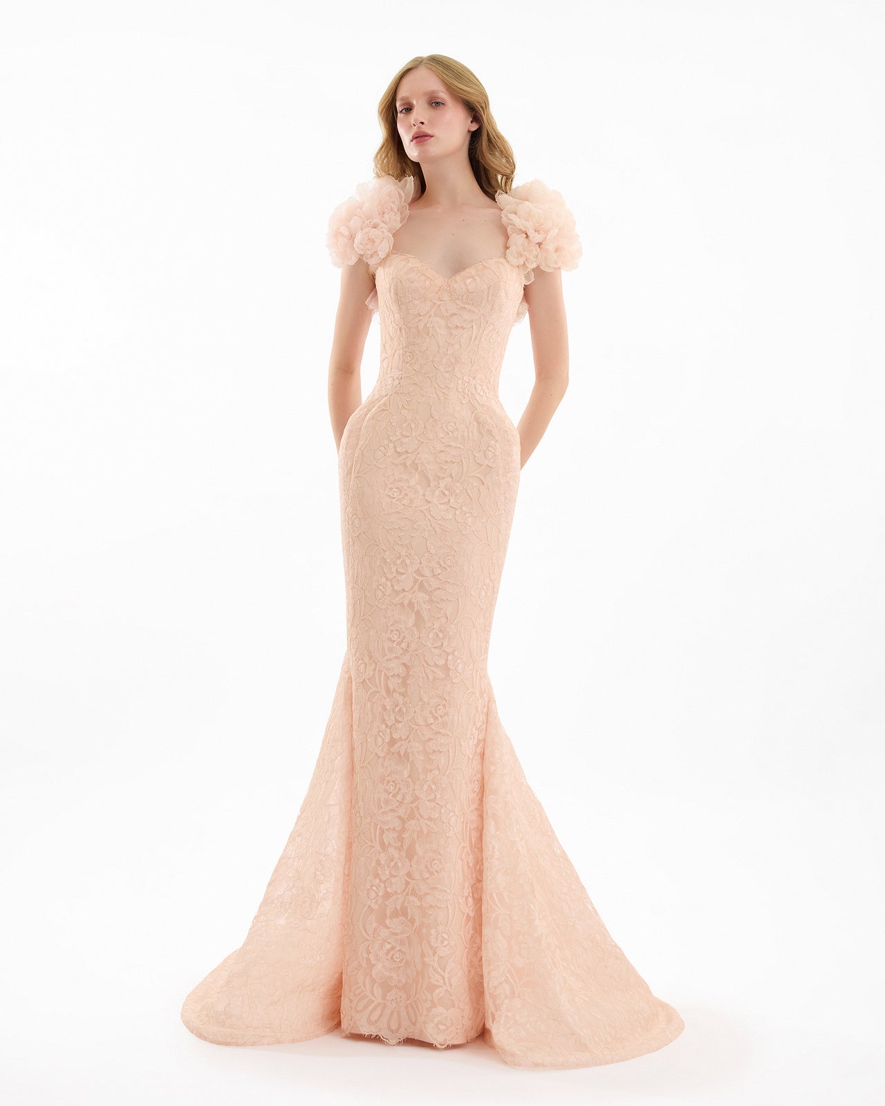 Woman wearing a blush pink evening gown with floral details on a white background