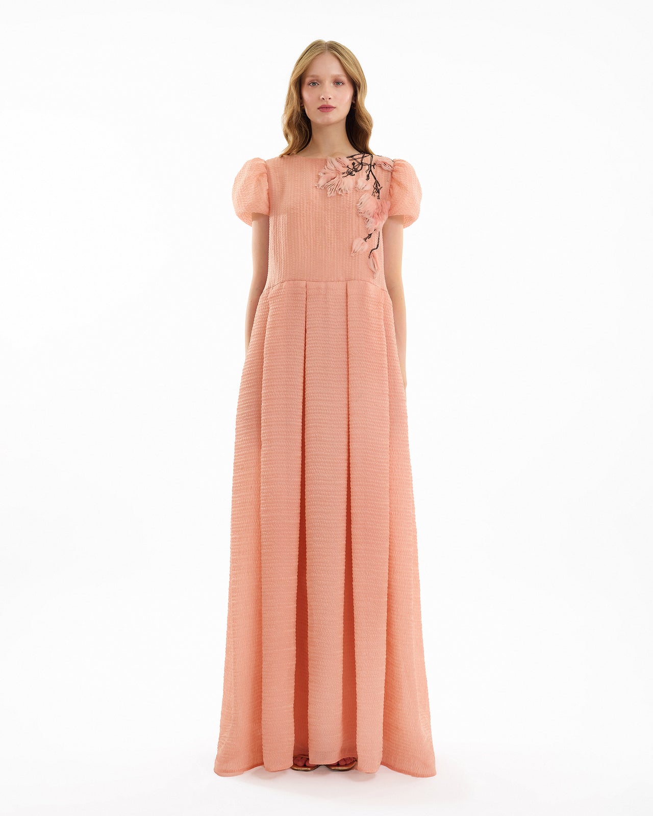 Woman wearing a long peach dress with floral embroidery on a white background