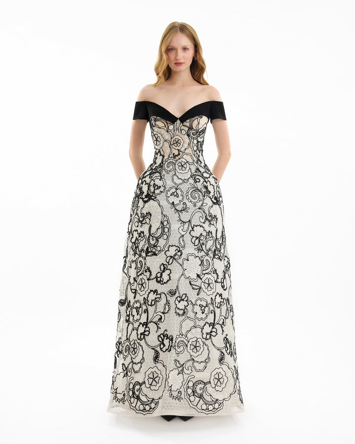 Woman wearing a black and white floral off-shoulder gown on a white background
