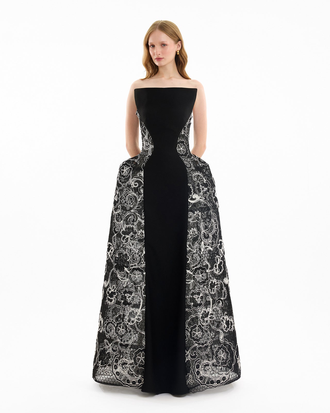 Woman wearing a black strapless gown with intricate white lace detailing on a white background