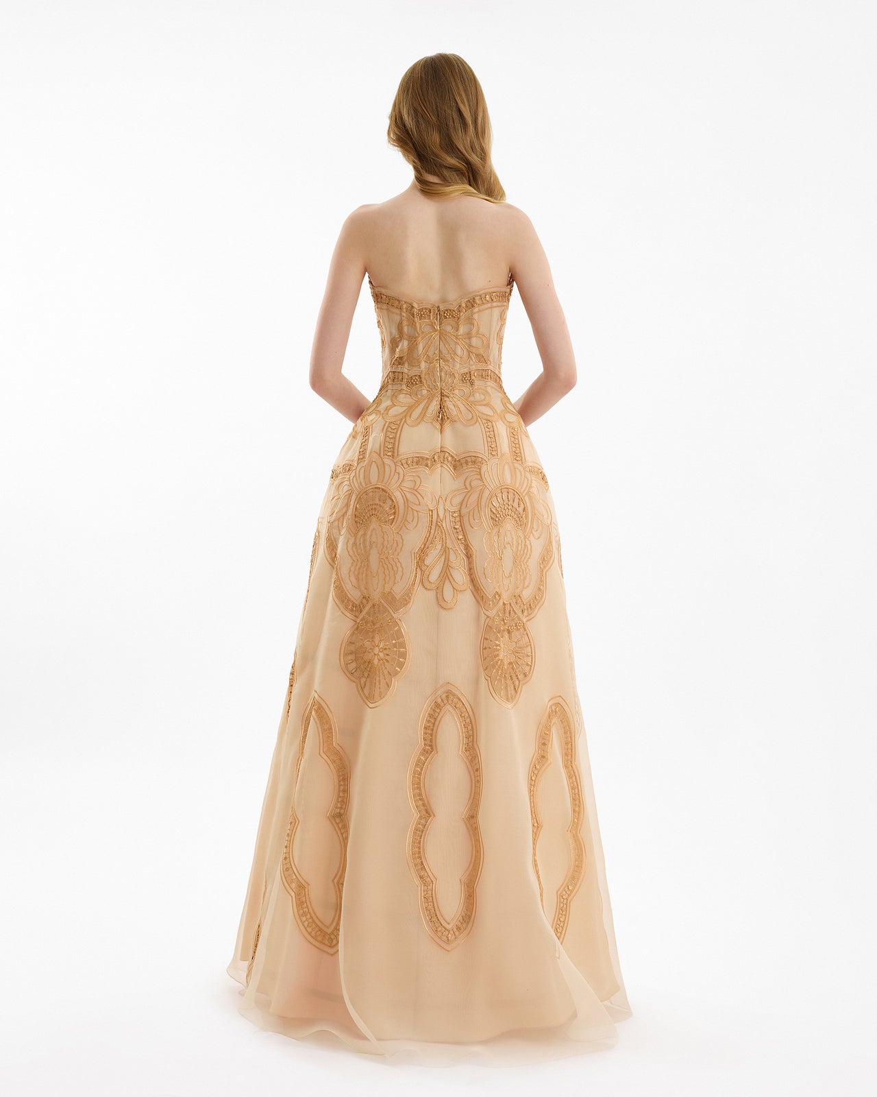 Woman wearing a gold strapless gown with intricate designs on a white background