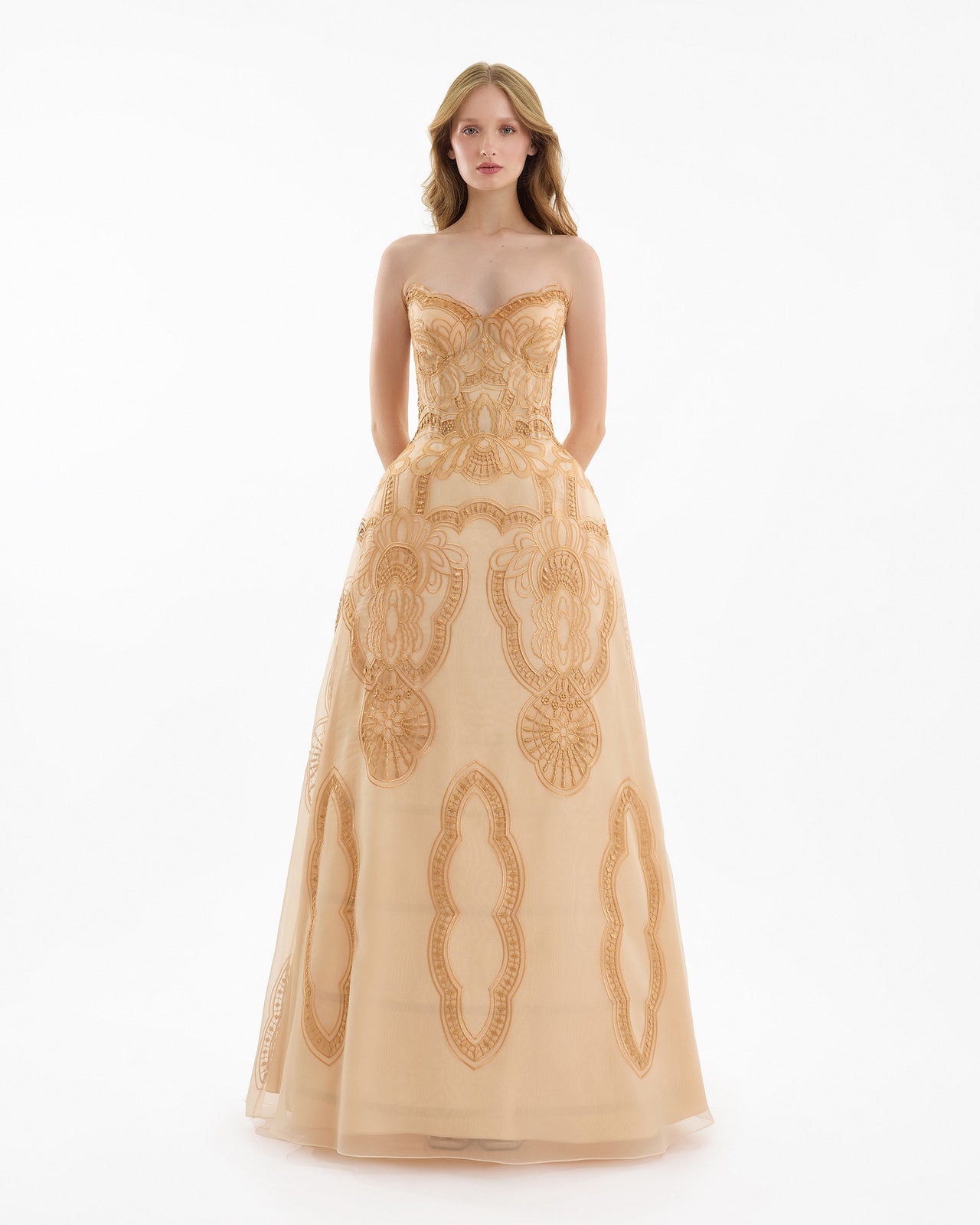 Woman wearing a beige strapless gown with intricate gold embroidery on a white background